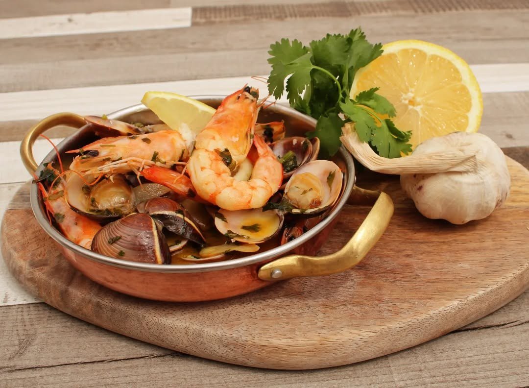 Frutos do mar à Bolhão Pato numa caçarola de cobre, com camarão, amêijoas, limão e ervas, sobre uma tábua de madeira